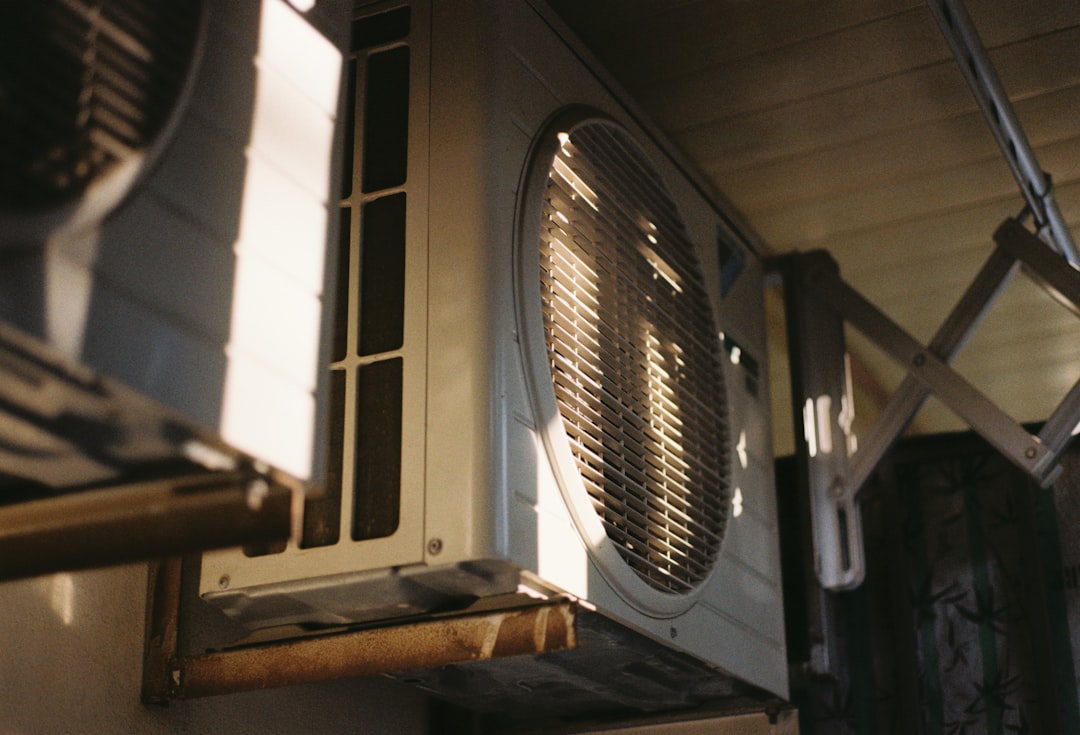 An outdoor heat pump condenser unit against a sunny exterior wall