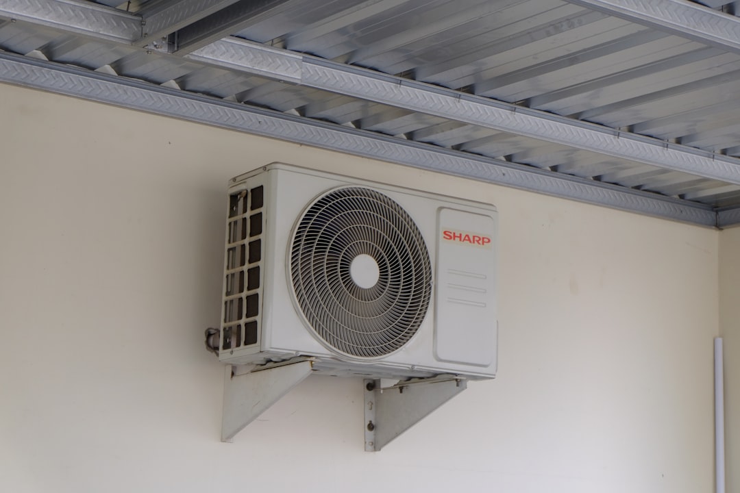An air conditioning outdoor condenser unit mounted on a wall beside a building