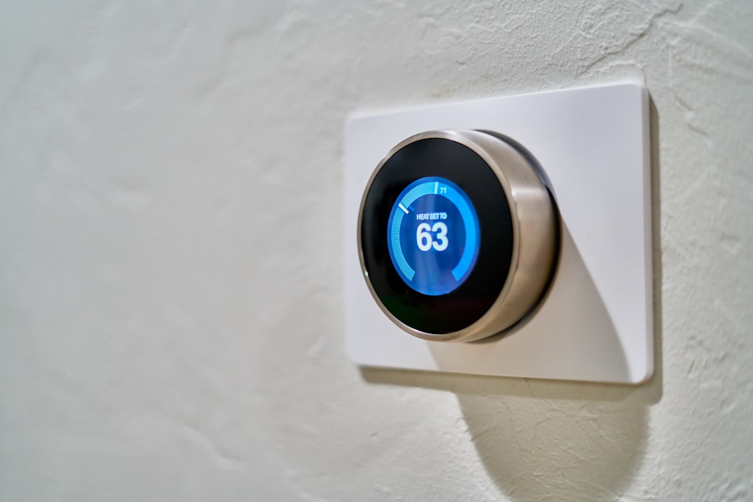 Gray Nest smart thermostat mounted on wall displaying temperature at 63 degrees